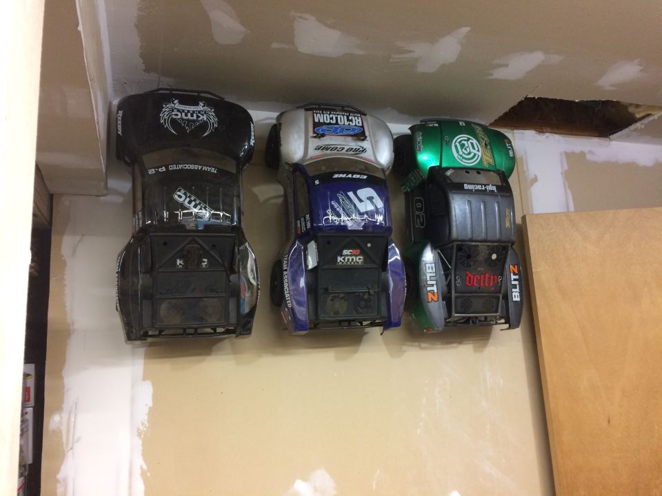 Three remote control car bodies hanging on a wall. Black, purple, and green bodies are visible