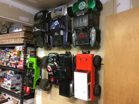 1989 Ford Bronco - A collection of RC monster trucks is displayed on a wall above shelves filled with model car boxes.