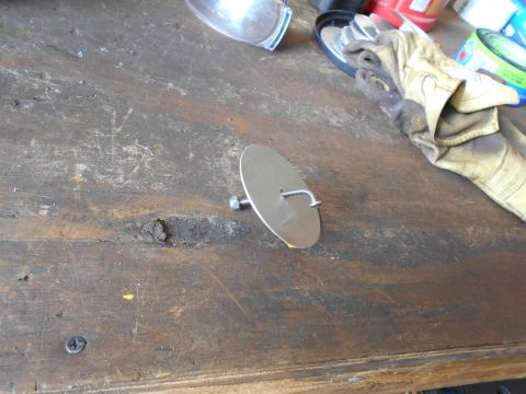 1992 Ford Bronco - A metal disc with a bolt and hook is on a workbench next to work gloves and other items.