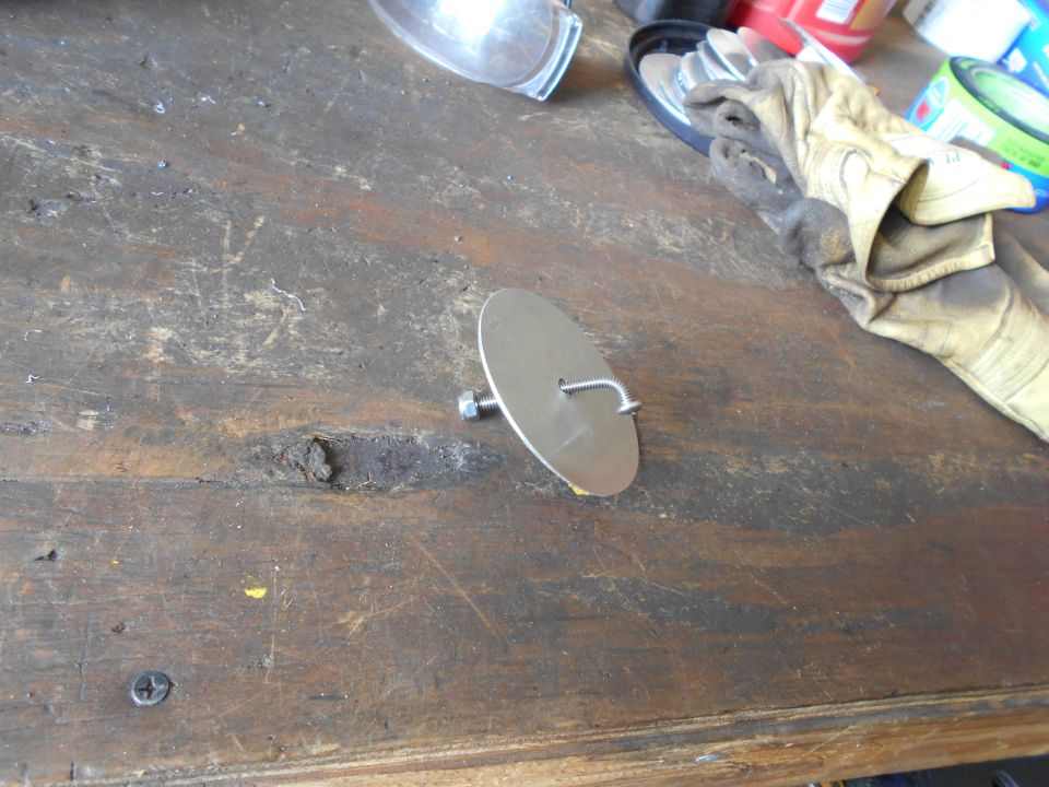 Metal disc with a bolt and hook attached, lying on a wooden workbench