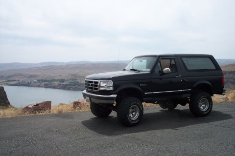 1995 Ford Bronco - A black Ford Bronco is parked on a scenic overlook next to a body of water.