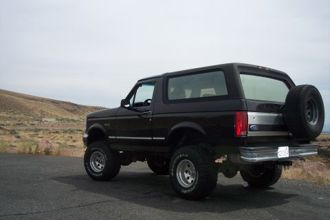 1995 Ford Bronco - A lifted black Ford Bronco is parked on a road with a spare tire on the back, under a cloudy sky.