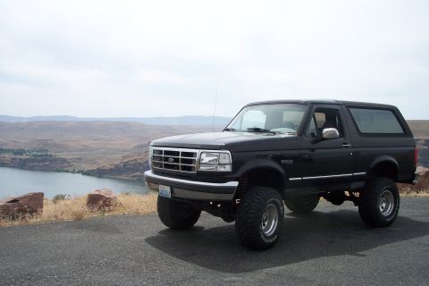 1995 Ford Bronco - Lifted 1995 Ford Bronco parked on a cliff with a river and mountains in the background.