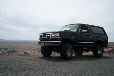 1995 Ford Bronco - A lifted black Ford Bronco is parked on the side of a road with a vast, dry landscape stretching out behind it.