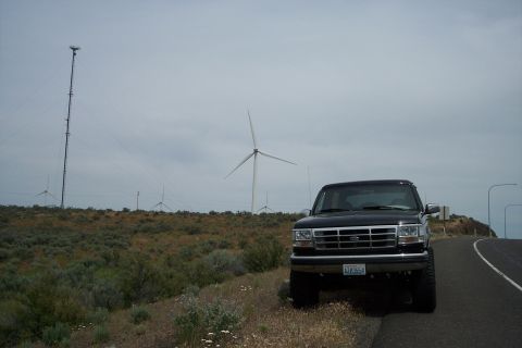 1995 Ford Bronco - A black 1995 Ford Bronco is parked on the side of a road, with wind turbines visible in the distance under a cloudy sky.