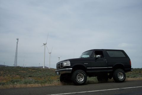 1995 Ford Bronco - Black 1995 Ford Bronco parked roadside with wind turbines and a tower in the distance.
