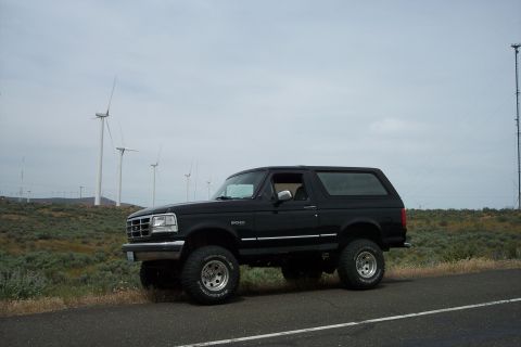 1995 Ford Bronco - A lifted black Ford Bronco is parked on the side of a road with wind turbines visible in the distance.