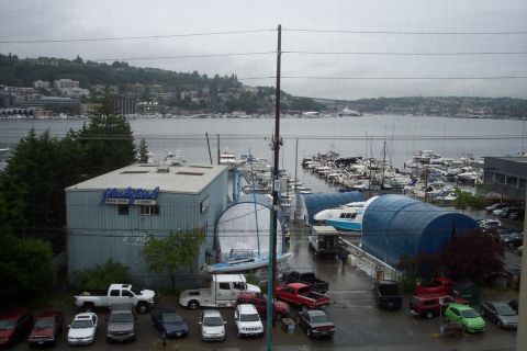 1995 Ford Bronco - A marina scene shows multiple vehicles and boats docked, with buildings and a distant cityscape under an overcast sky.