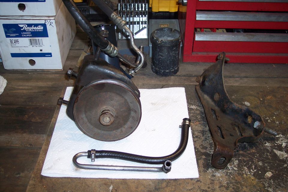 Disassembled power steering pump and bracket on a wooden surface.