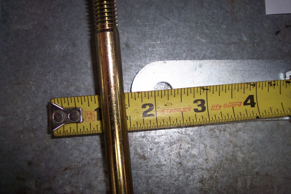 Brass bolt measured with a yellow Stanley tape measure on a metallic surface.