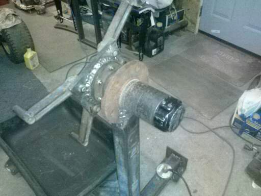 Trailer axle assembly with brake rotor and hub on a stand in a workshop.