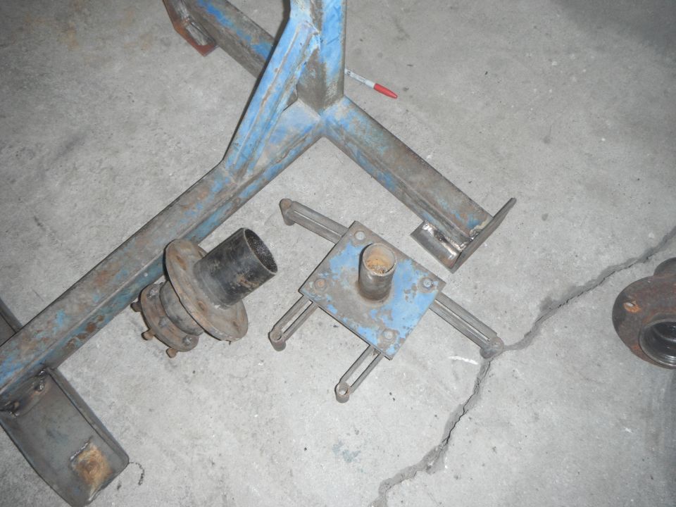 Metal parts including a blue frame, wheel hub, and rusty component on concrete.
