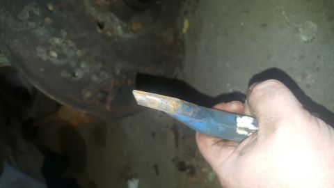 1995 Ford Bronco - A close-up of a hand holding a rusty blue pry bar near a heavily corroded brake rotor or similar vehicle part.