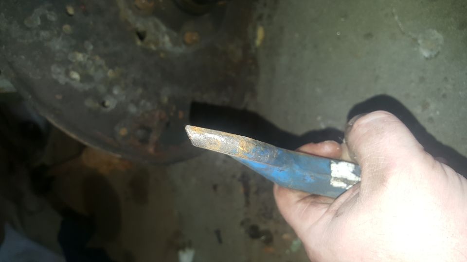 Hand holding a rusty blue pry bar near a corroded vehicle part.