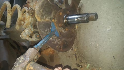 1995 Ford Bronco - A close-up view shows a mechanic using a pry bar and hammer to work on a rusty suspension component and brake rotor assembly, with a spline…