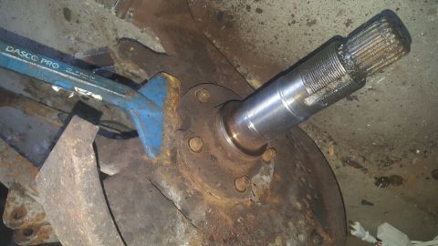 1995 Ford Bronco - A close-up view shows a splined shaft extending from a rusty hub assembly, secured by bolts. A blue pry bar is used to apply leverage to th…