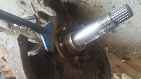 1995 Ford Bronco - A close-up shot shows a splined axle shaft being worked on with a blue pry bar. The scene appears to be a mechanic's workspace with rusty m…