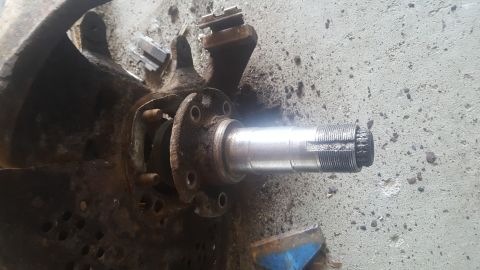 1995 Ford Bronco - A close-up view of a rusty automotive spindle and hub assembly resting on a concrete surface. The spindle has visible threads and a damaged…