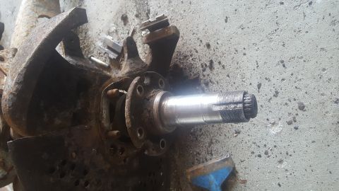 1995 Ford Bronco - A rusty, disassembled vehicle spindle assembly is shown on a concrete surface. The spindle has splines on the end and a flange with bolt ho…