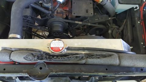 1978 Ford Bronco - Close-up view of a damaged foam insulation piece in front of a vehicle's radiator and engine components. The radiator cap is visible and sh…