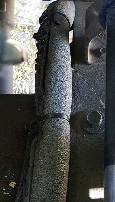 1978 Ford Bronco - A close-up view shows a heavily insulated hose or conduit secured with a black zip tie, mounted to a dark, textured surface. The insulation…