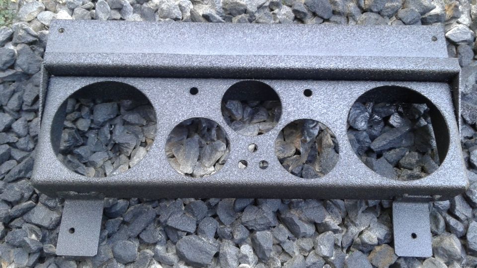 Dark gray metal speaker bracket with circular cutouts on gravel