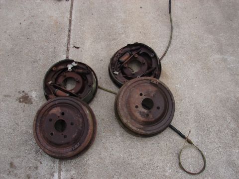 1973 Ford Ranchero - Two pairs of rusty brake drums and brake shoes are laid out on a concrete surface. One pair is assembled, with brake shoes and springs visi…