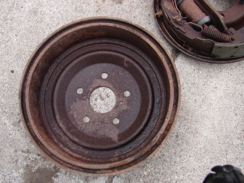 1973 Ford Ranchero - A rusty brake drum and brake shoes are shown resting on a concrete surface. The brake drum is in the foreground, with the brake shoes visib…