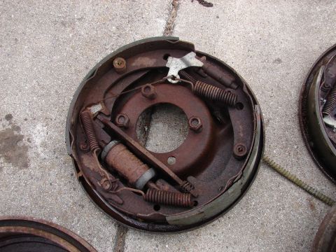 1973 Ford Ranchero - A pair of rusty drum brake assemblies are laid out on a concrete surface. One assembly is in focus, showing brake shoes, springs, and a whe…