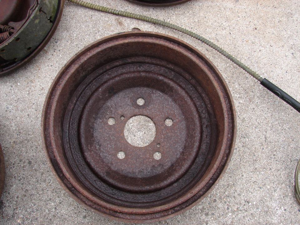 Two rusty brake drums and a brake cable on concrete.