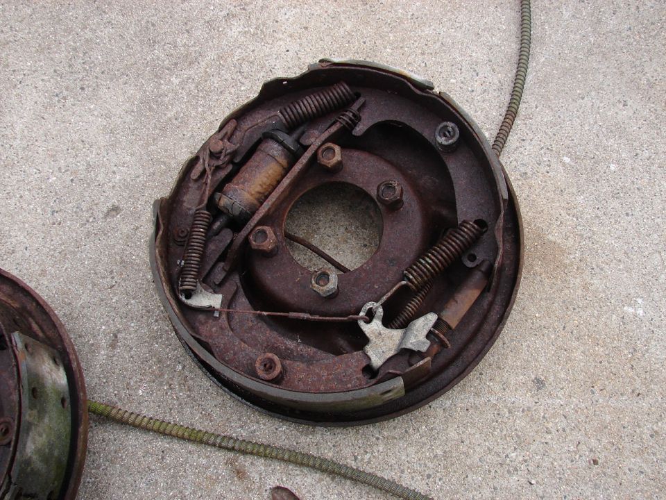 Rusted drum brake assembly with brake shoes, springs, and cable on concrete