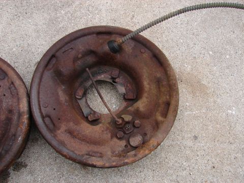1973 Ford Ranchero - Two heavily rusted brake drums are shown resting on a concrete surface. One drum is in the foreground and has a brake cable attached.