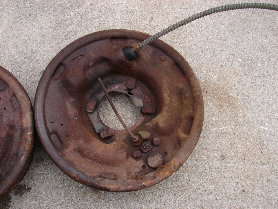 Two rusted brake drums, one with a brake cable, on concrete.