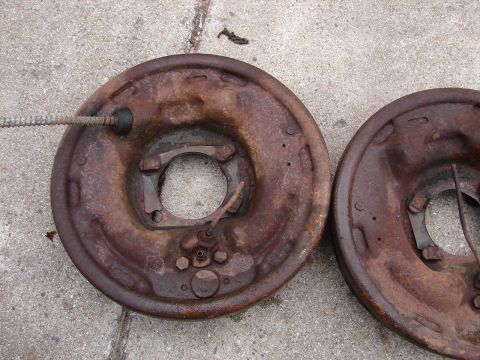 1973 Ford Ranchero - Two heavily rusted brake drums are shown lying on a concrete surface. A braided metal cable housing is attached to the drum on the left.