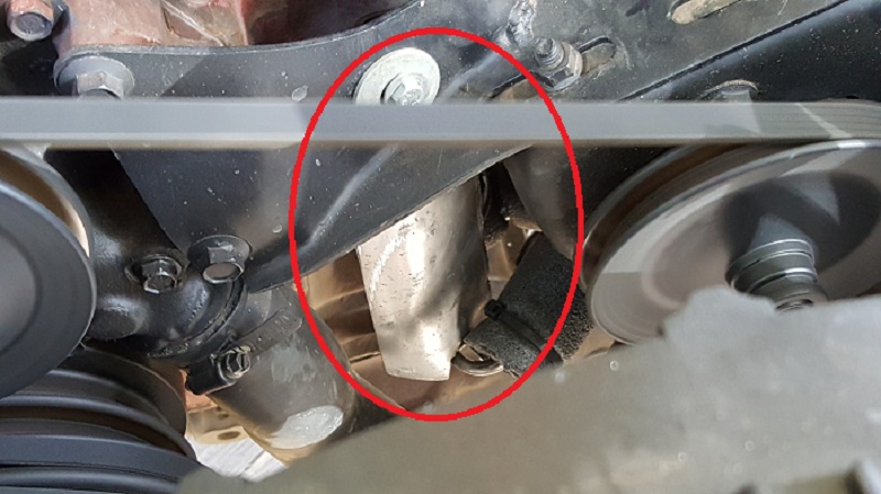 Close-up of vehicle engine serpentine belt and pulleys, with a red circle around a metal component.
