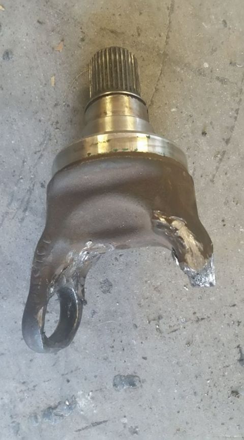 1979 Ford Bronco - Driveshaft slip yoke with a splined output stub and U-joint ears, smeared with grease, lying on a concrete floor.