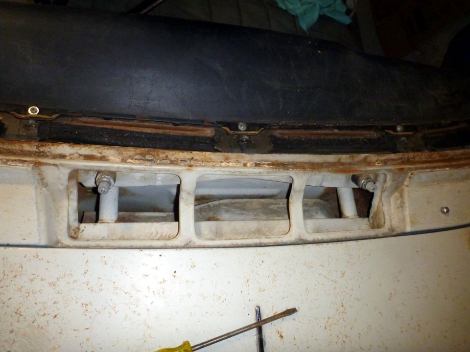 Close-up of vehicle dashboard with openings, bolts, and rust.