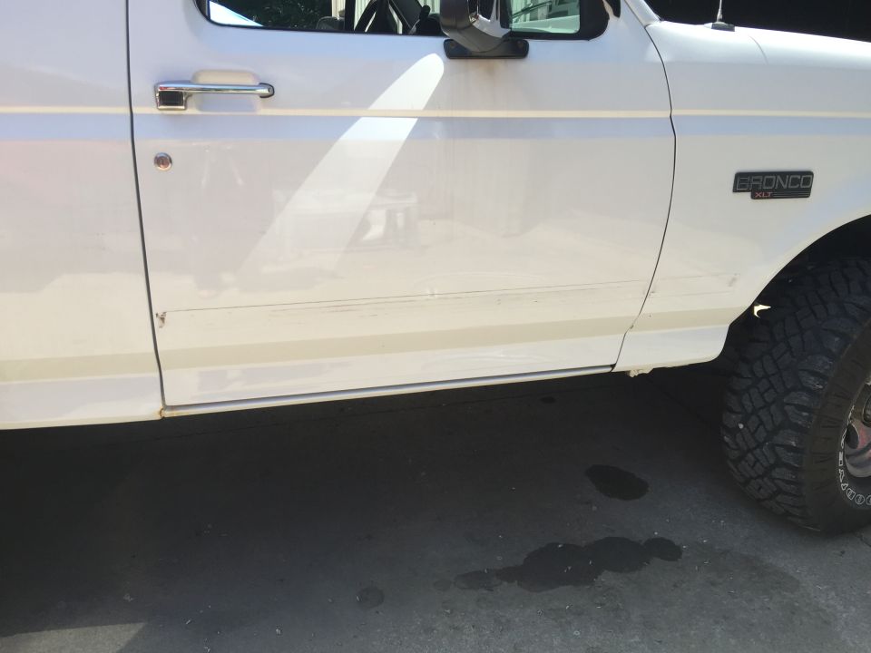 White Ford Bronco driver's side door and fender with visible scratches and rust.