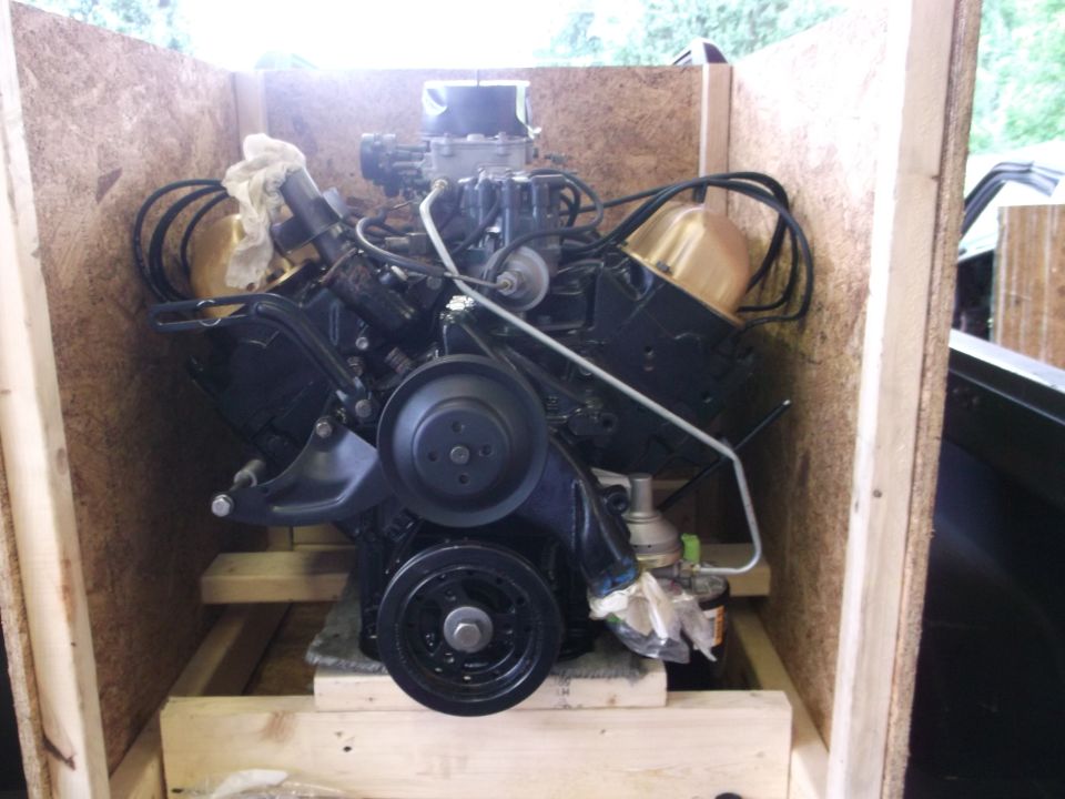 Black V8 engine with gold valve covers in a wooden crate.