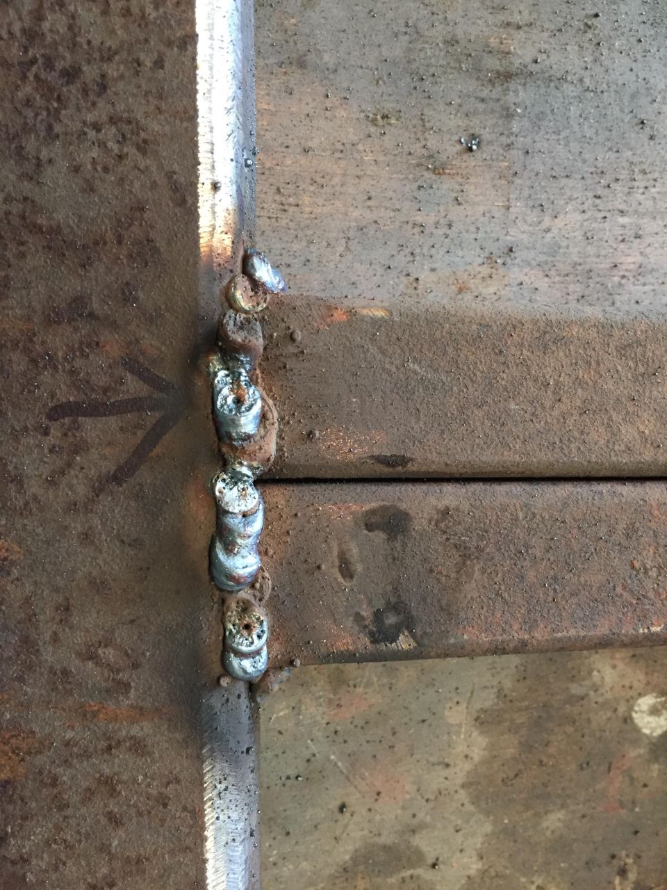 Close-up of a weld on rusty metal with a black arrow.