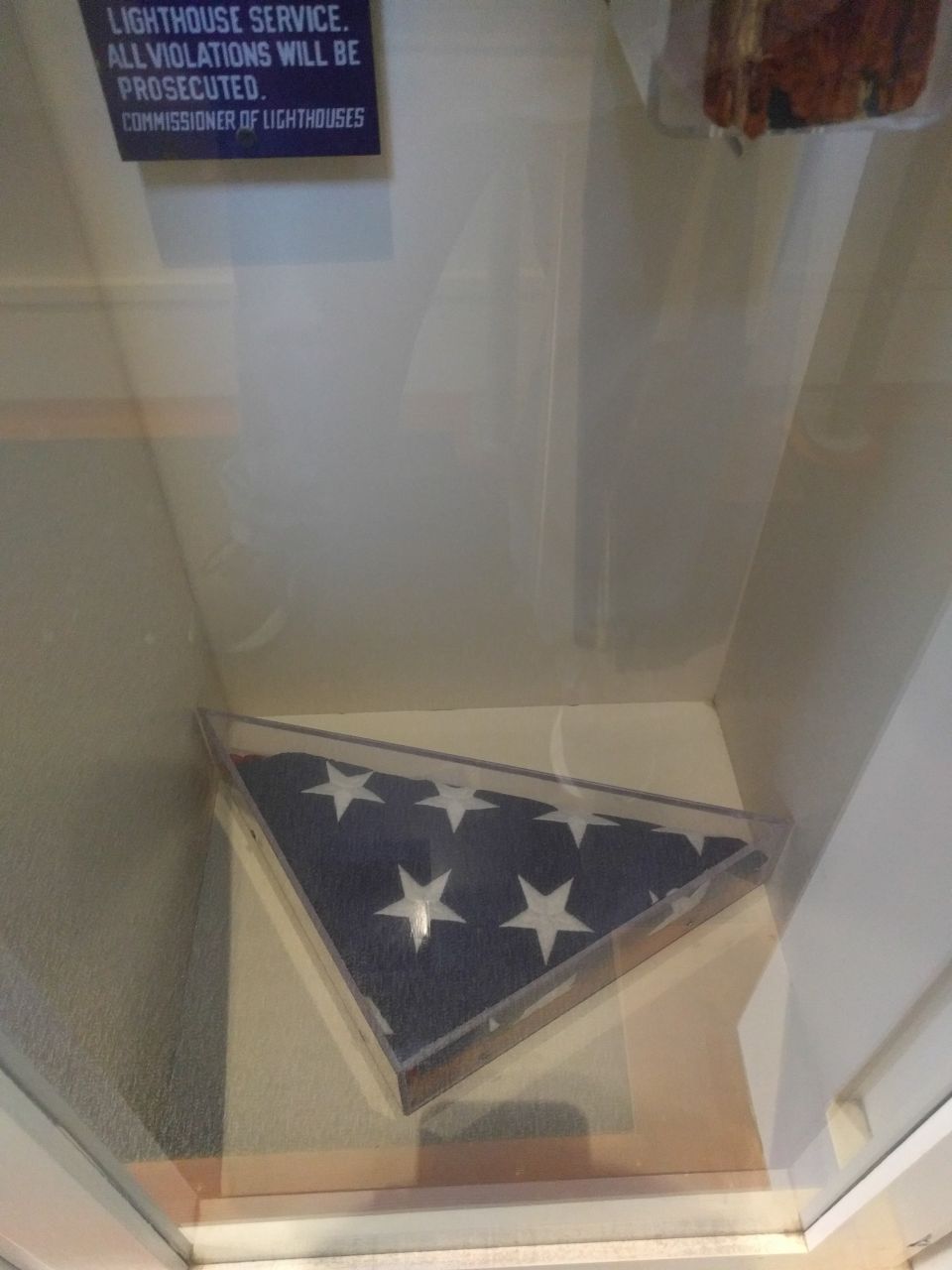 Folded American flag in a display case with a lighthouse service sign.