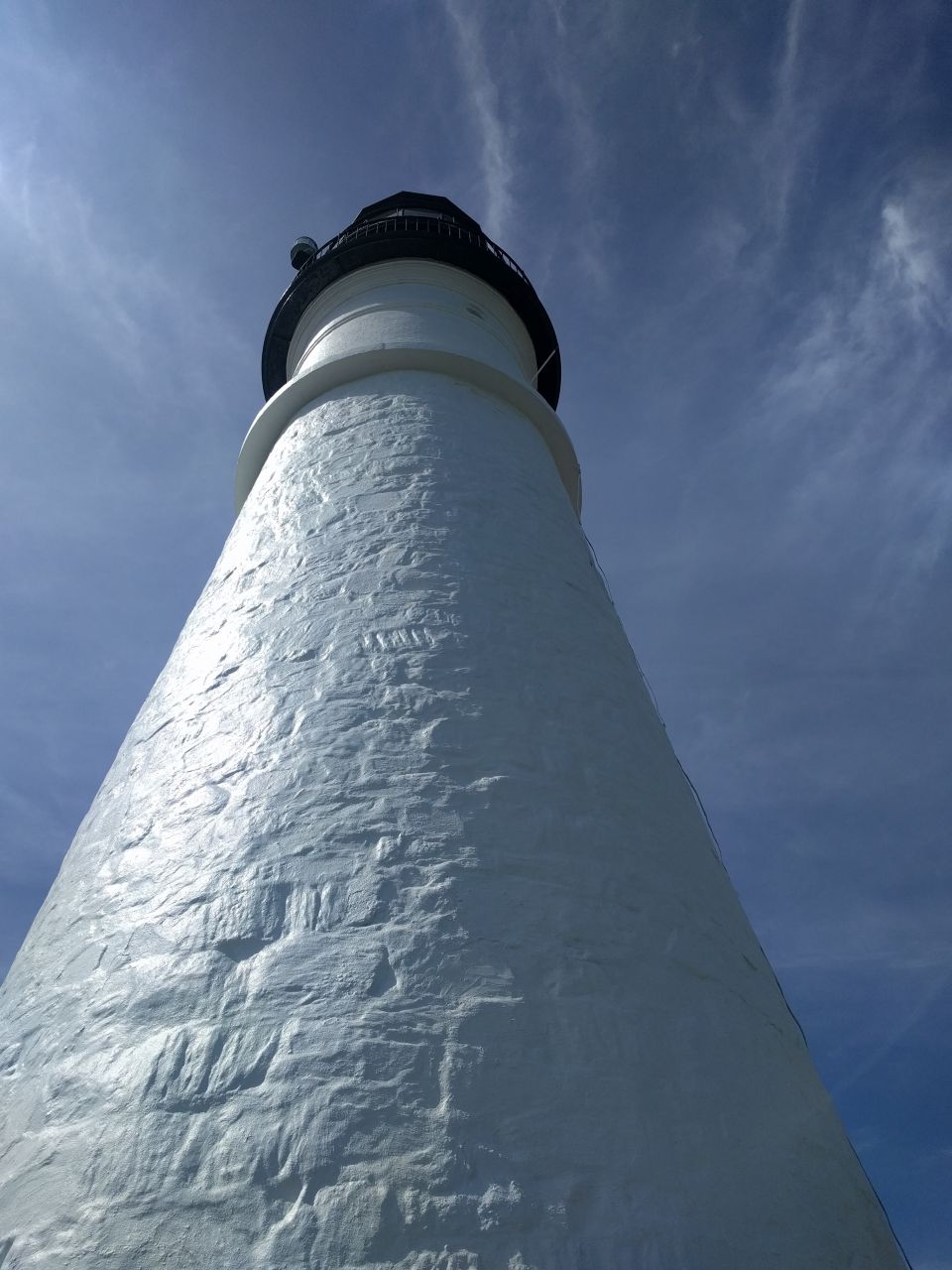 White lighthouse against a blue sky with wispy clouds.