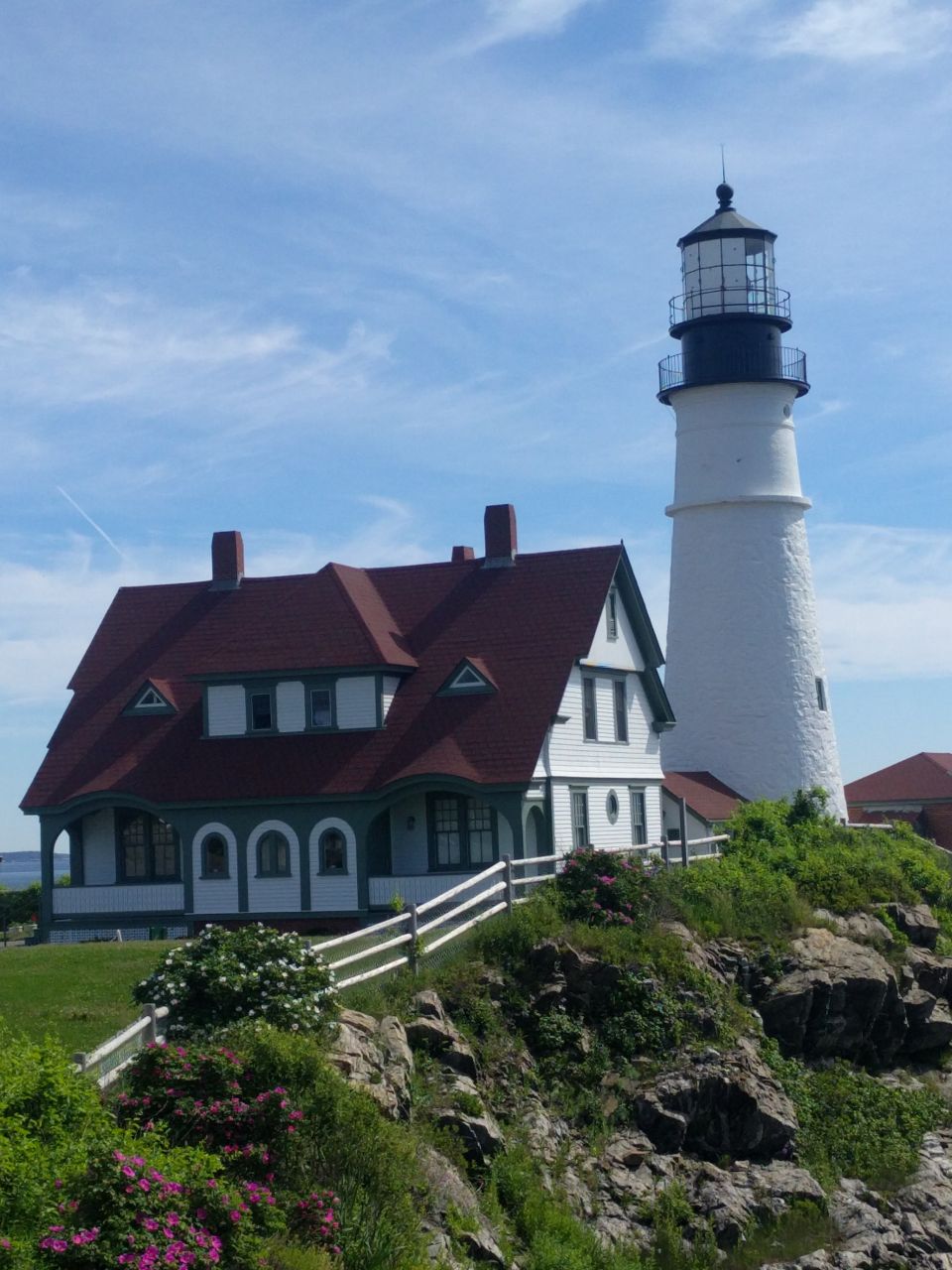 White lighthouse and house on a rocky coast with blue sky and clouds.
