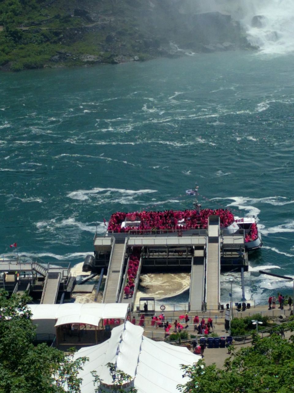 Tour boat with many passengers in red ponchos approaching a dock near a waterfall.