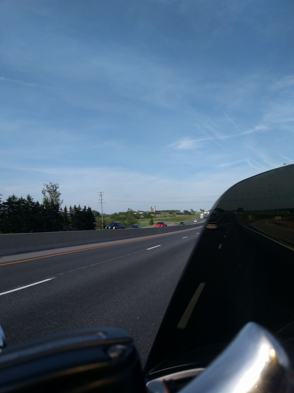 Motorcycle windshield reflecting a highway with cars, under a blue sky.