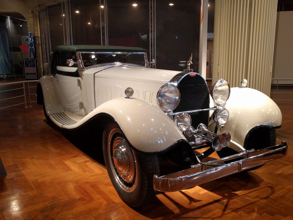 White vintage Bugatti convertible with green top, chrome accents, on wooden floor.