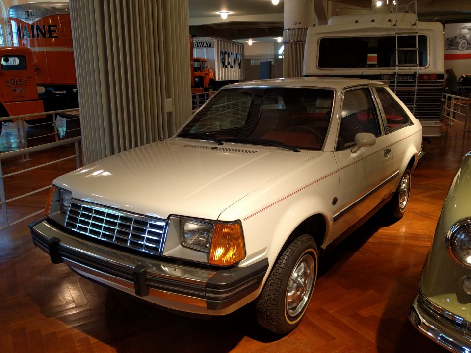 White 1980s hatchback with chrome grille and orange turn signals parked indoors.