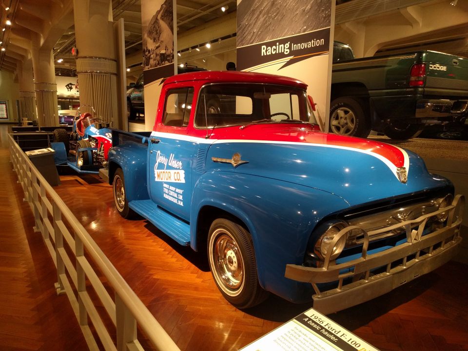 1956 Ford F-100 pickup truck, blue and red, with "Jerry Unser Motor Co." on the door, displayed in a museum.
