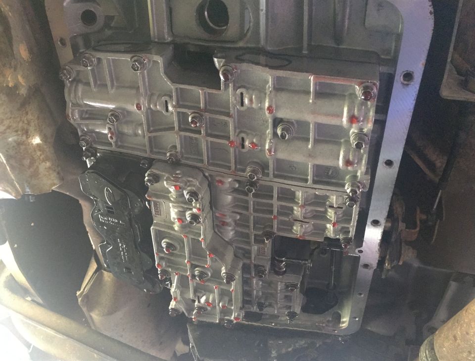 Underside of a vehicle showing a transmission pan with a new gasket and bolts.