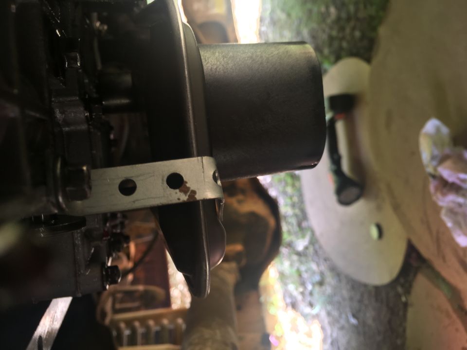 Close-up of a black metal part secured by a silver bracket, with a blurred outdoor background.